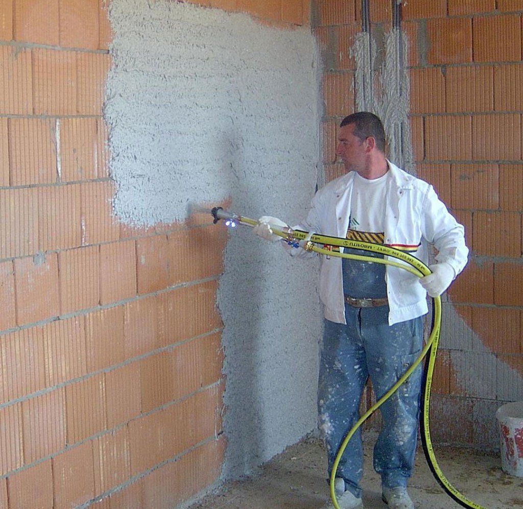 Team applying machine-sprayed plaster to internal masonry walls