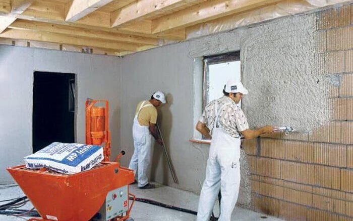 Plasterers spraying gypsum plaster onto internal block walls using a plastering machine